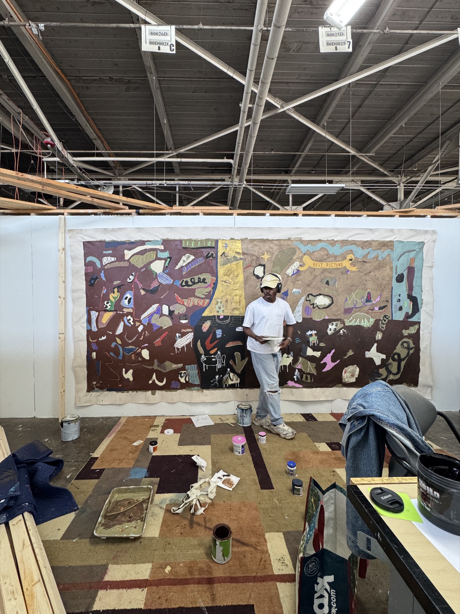 Bhare at work in a warehouse studio, a wide unstretched canvas pinned to the wall behind him